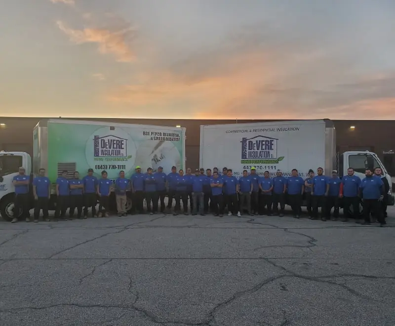 Many members of the DeVere Home Performance team standing outside in front of two company trucks.