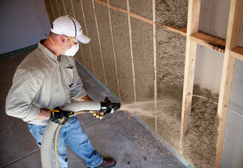 Worker applying damp spray Cellulose insulation into open wall cavities.