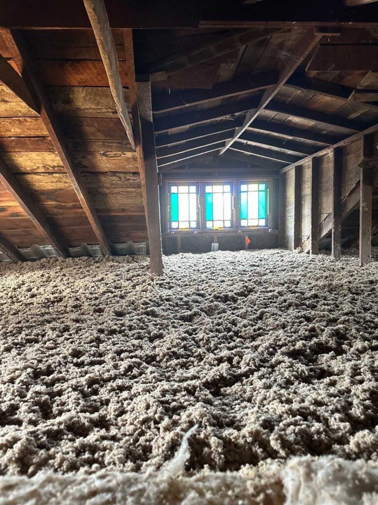 Cellulose blown insulation being applied in an attic by DeVere Insulation Home Performance, illustrating a meticulous installation designed to improve energy efficiency and reduce heat loss.