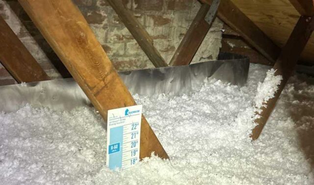 Attic with blown-in insulation, measuring guide, wooden beams, and exposed brick walls.