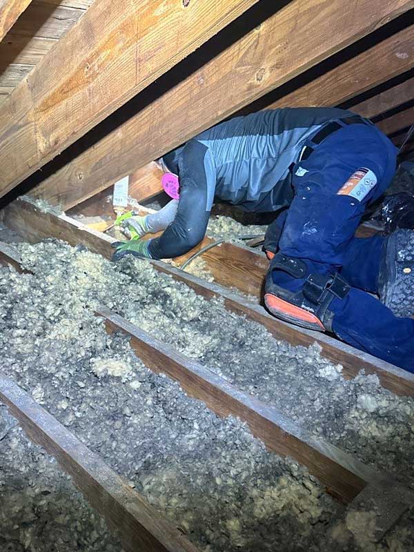 Image of technician air sealing attic in residential home: A trained DeVere Insulation technician applies air sealing foam around attic penetrations to prevent energy loss and improve home comfort.