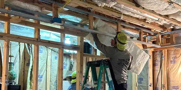 Close-up of a skilled DeVere Insulation Home Performance employee fitting batt insulation into ceiling framing, optimizing heat retention and energy savings.