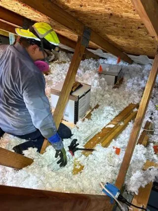 Insulating Around Recessed Lights: A technician carefully insulating around recessed light covers in the attic to prevent air leaks and improve energy efficiency.