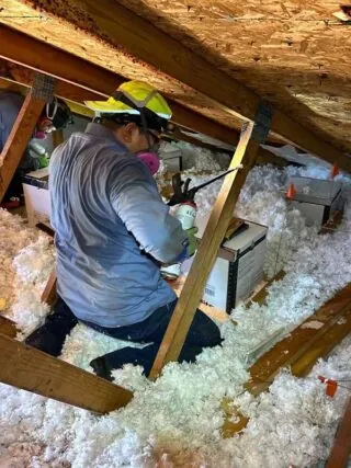 Sealing Recessed Lights for Energy Efficiency: Proper insulation being applied around recessed light fixtures in an attic to minimize heat loss and ensure a more comfortable home environment.