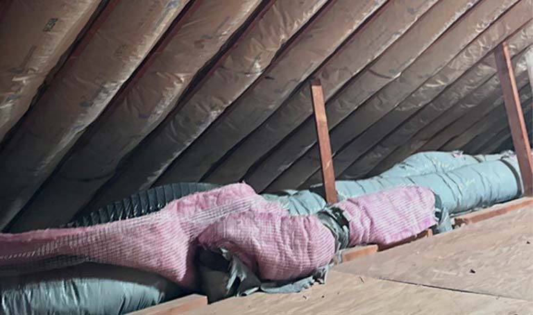 Close-up view of attic roofline featuring installed kraft-faced fiberglass batt insulation fitted between wooden ceiling joists.