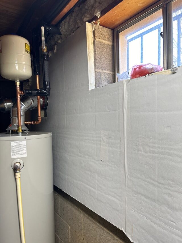 Rigid foam boards and spray‑foamed rim joist insulate a basement wall beside a water heater.