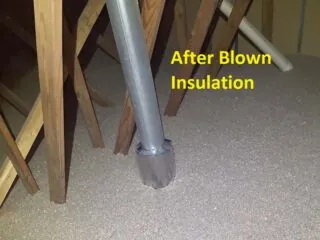 Freshly blown cellulose insulation surrounding a metal plumbing vent stack in an attic.