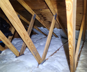 White fiberglass batts installed between attic joists with vent baffles along the roof deck.