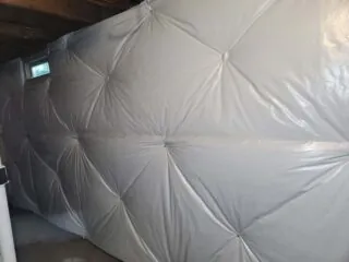 Basement wall covered with gray encapsulation blanket for vapor and thermal control.