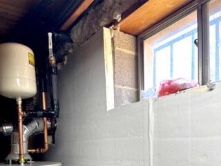 Foam-board blanket insulation installed on block wall behind water heater.