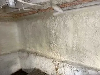 Spray foam insulated basement wall with exposed PVC drain line.