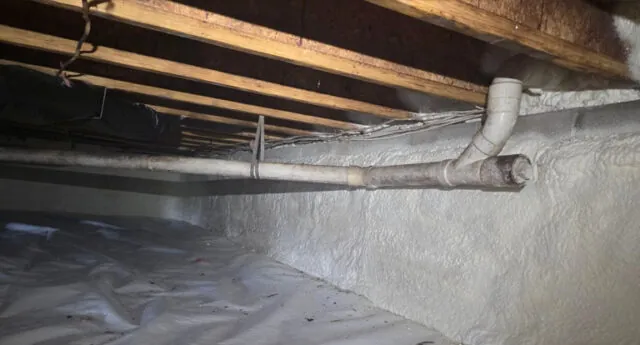 Crawl space with white vapor barrier on the floor and insulated pipes wrapped in protective covering.