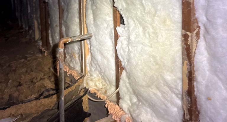 Fiberglass batt insulation installed on ceiling and walls in a residential construction site, covered with clear plastic vapor barrier.