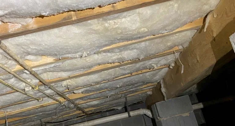 Knee wall insulation showing spray foam and batt layers installed between wooden studs in attic.