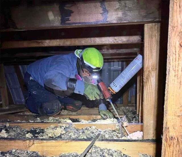 DeVere Insulation Home Performance technician air sealing a rim joist with caulk in a crawl space.